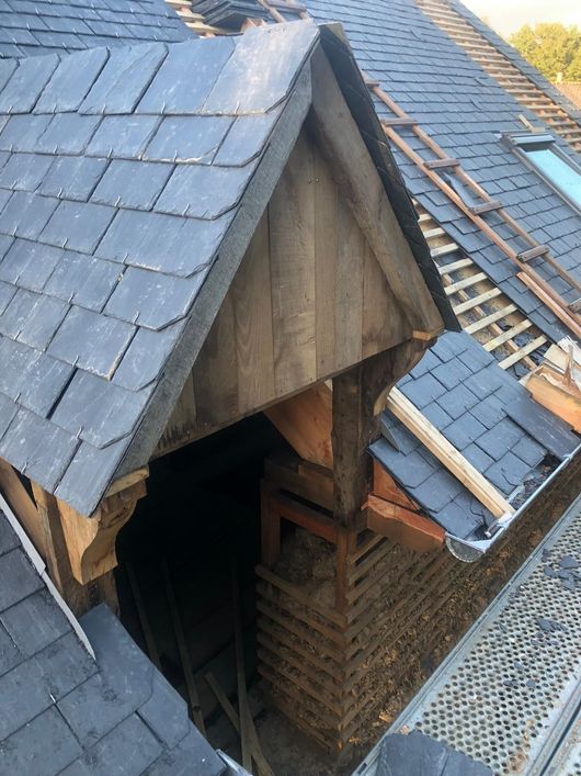 Vue en plongée d'un toit en construction, montrant une section de toit à pignon nouvellement recouverte de tuiles et une charpente en bois apparente.