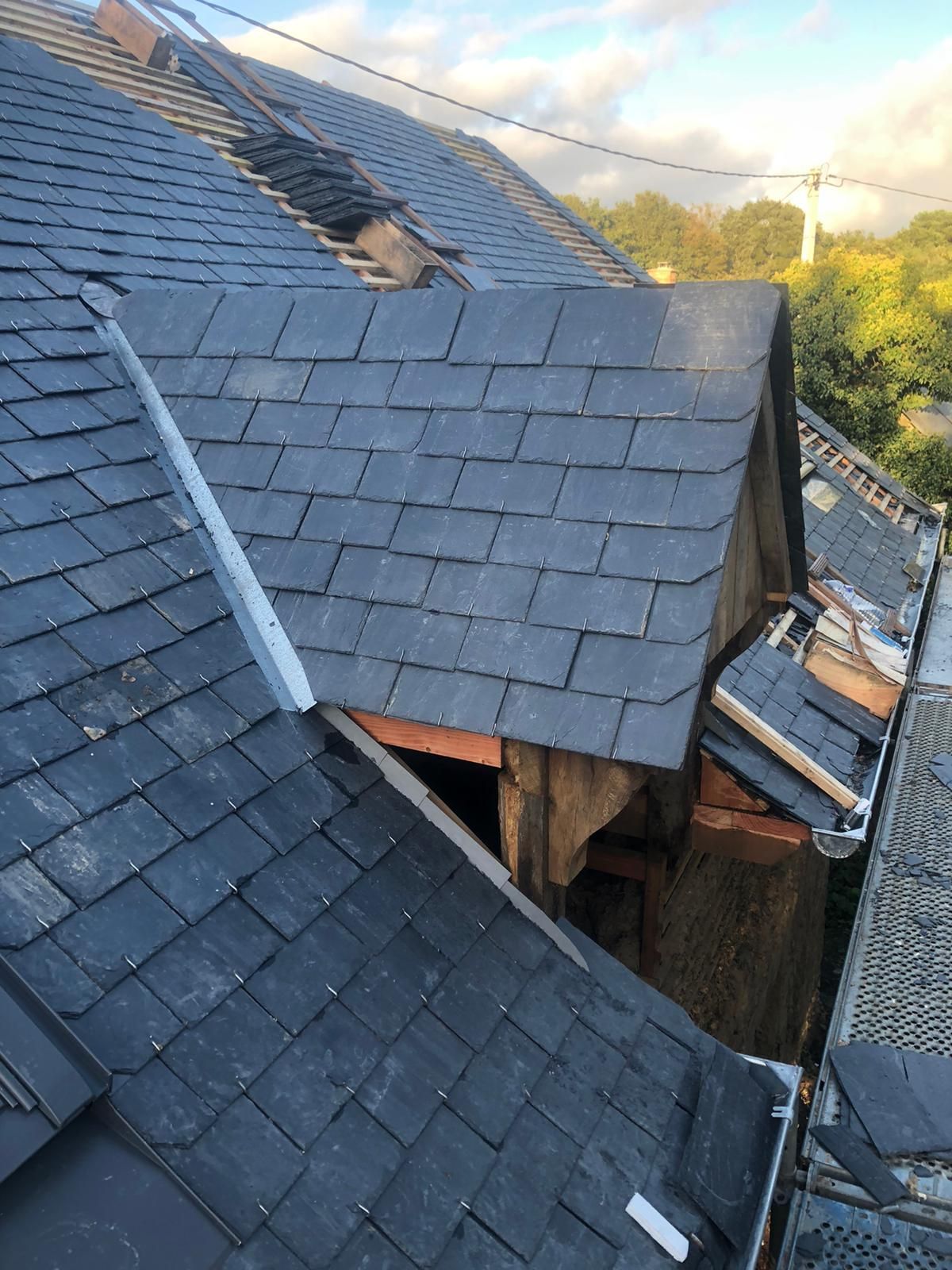 Gros plan sur un toit partiellement couvert de tuiles, avec une lucarne en construction, présentant des tuiles d'ardoise grise et du plomb.