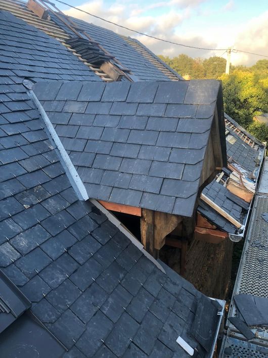 Vue aérienne d'un toit en ardoise en construction, montrant une section de lucarne avec une charpente apparente.