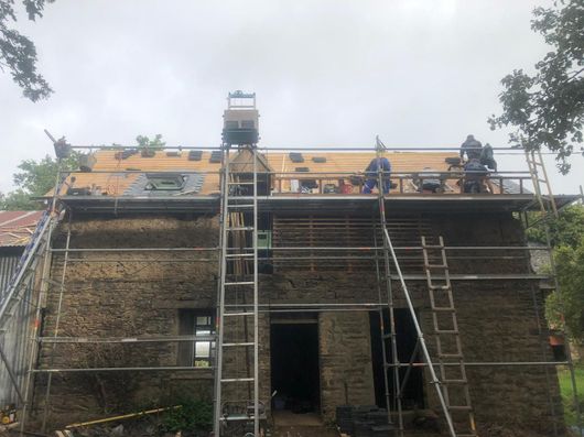 Des ouvriers se tiennent sur des échafaudages pour réparer le toit d'un bâtiment en pierre sous un ciel couvert.