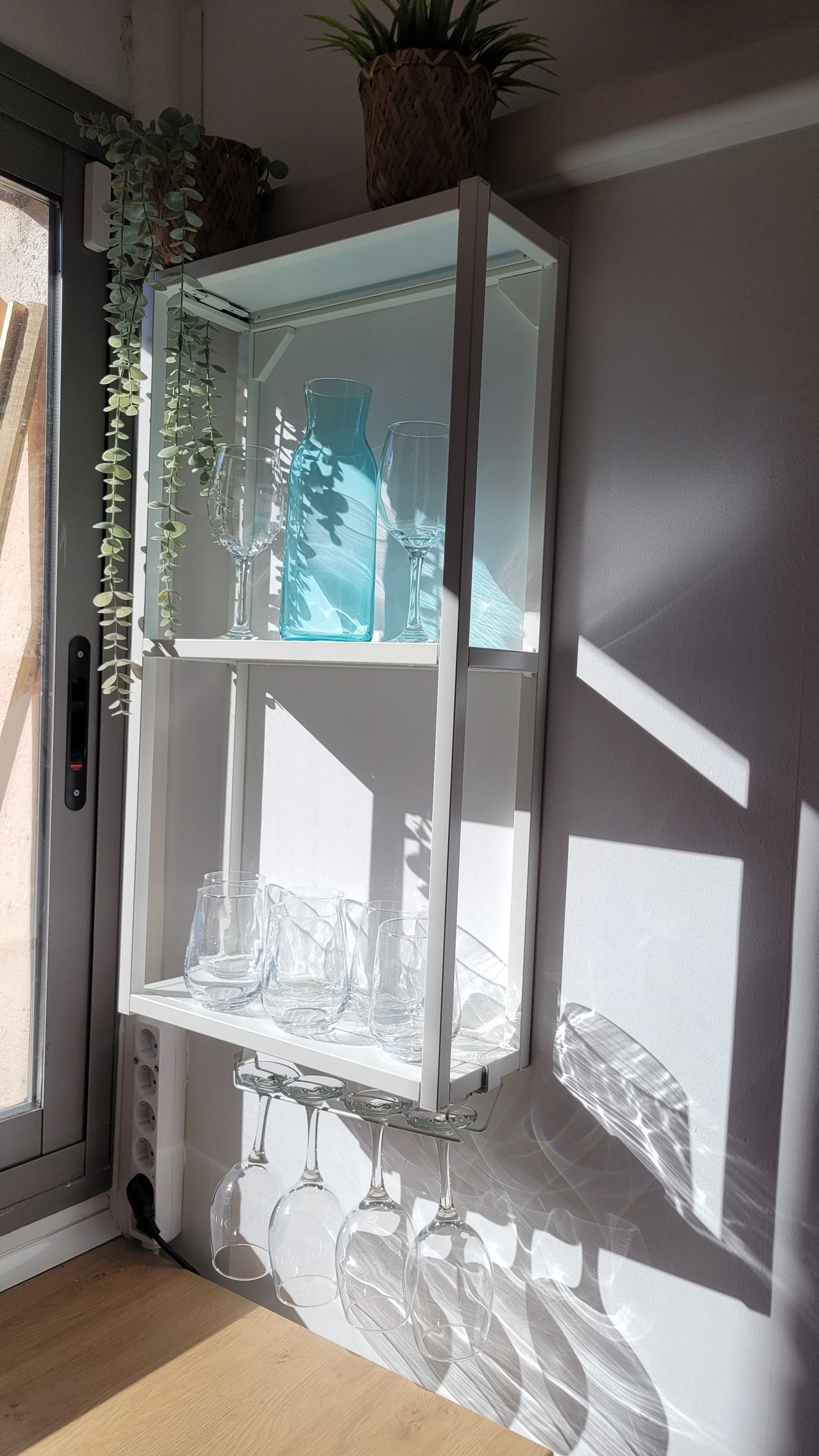 Un estante blanco con vasos encima en una habitación al lado de una ventana.