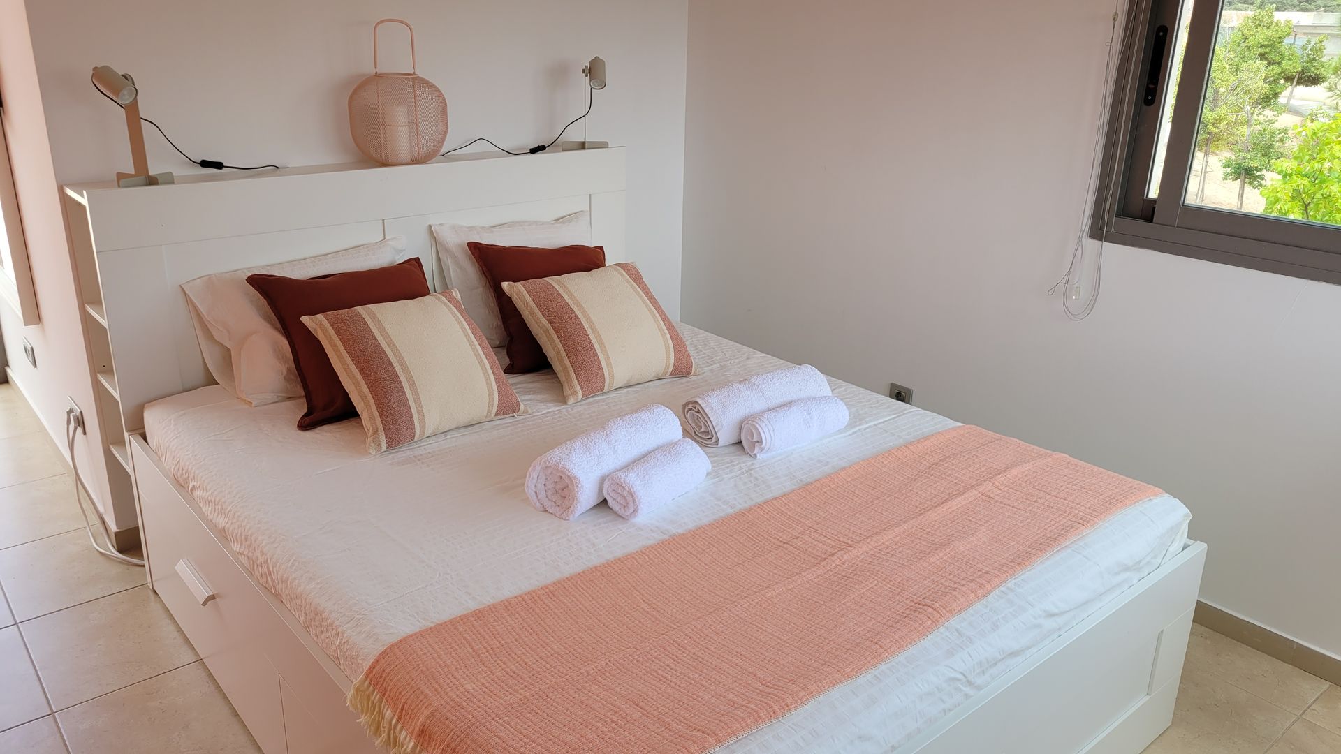 Un dormitorio con una cama, almohadas, toallas y una ventana.