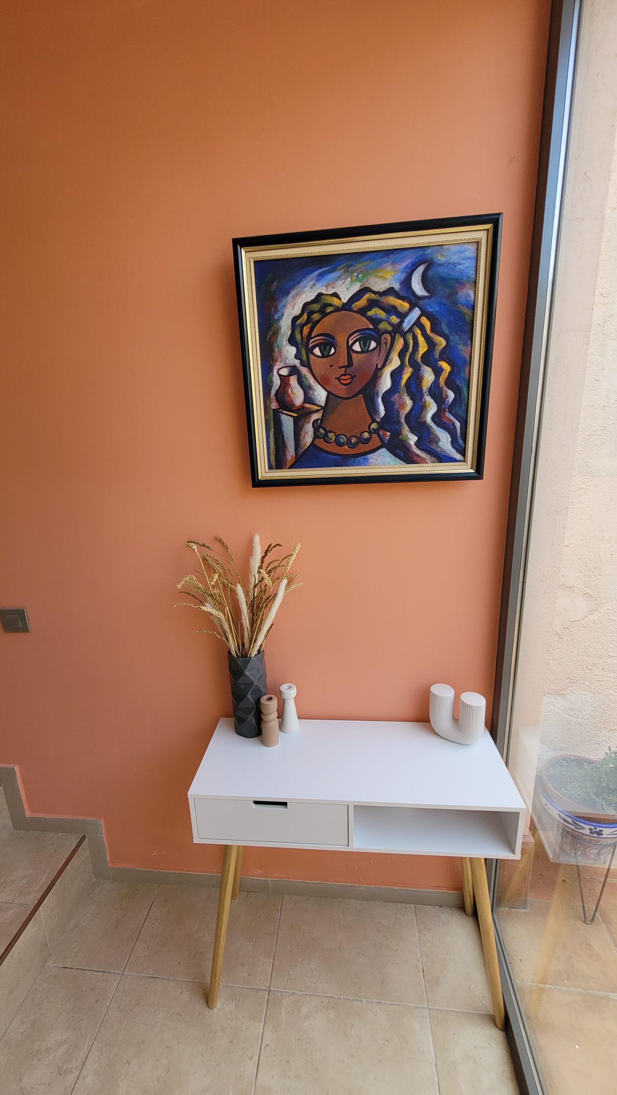 Hay un cuadro de una mujer en la pared encima de una mesa.