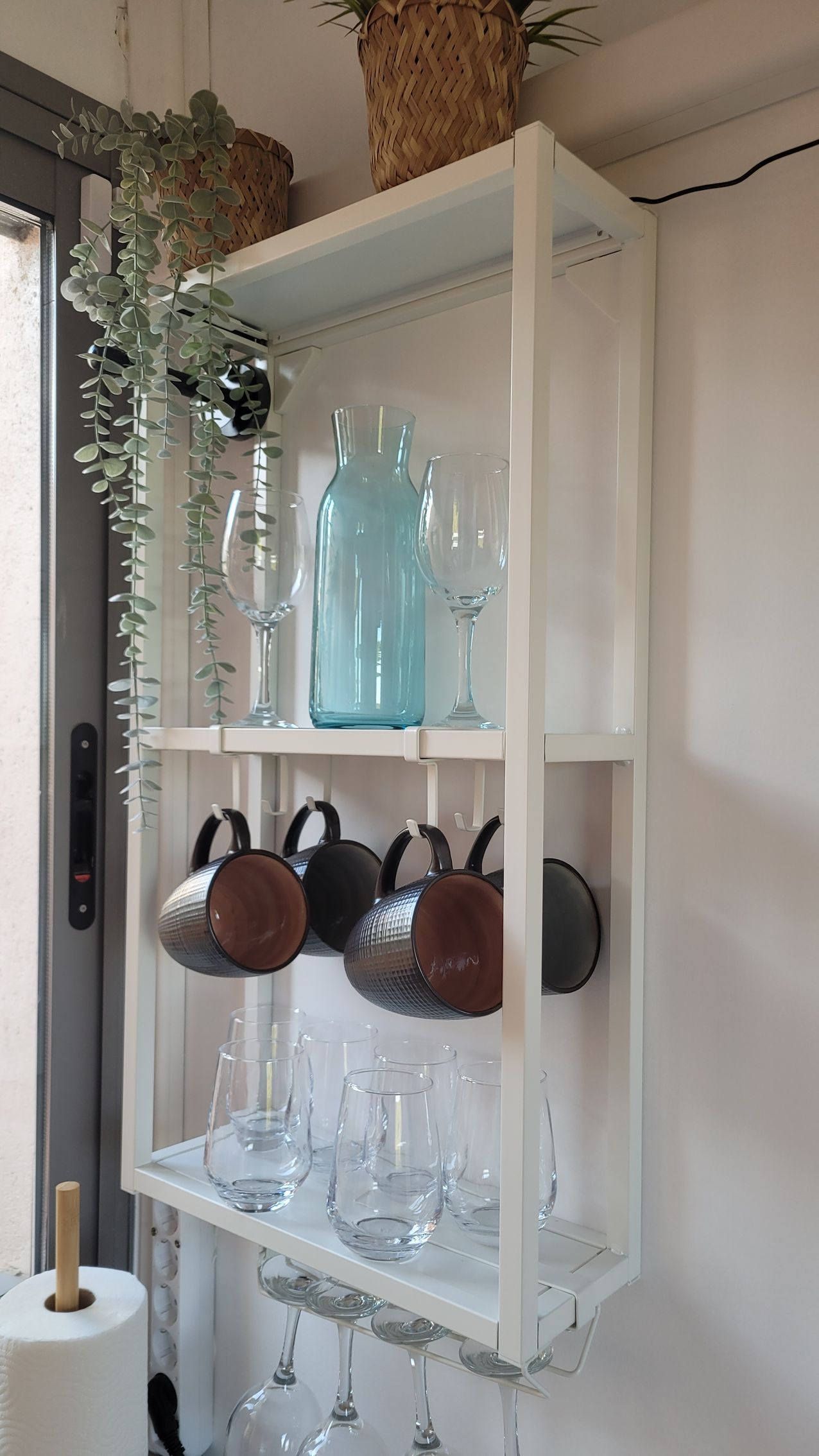 Un estante blanco con tazas y copas de vino encima.