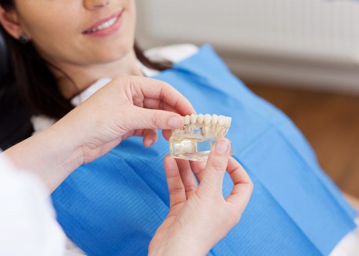 Un dentista sostiene un alineador dental transparente cerca de un paciente recostado con un babero azul.
