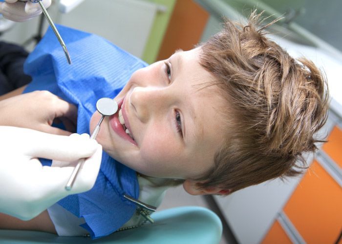 Paciente en el sillón dental recibiendo tratamiento del dentista, con guantes azules y herramientas a la vista.