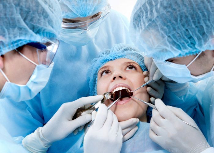 Los dentistas, vestidos con batas quirúrgicas azules, examinan la boca abierta de un paciente con instrumentos dentales.