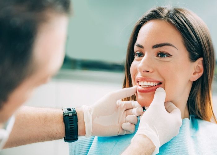 Dentista examinando los dientes de un paciente sonriente con manos enguantadas en una clínica luminosa.