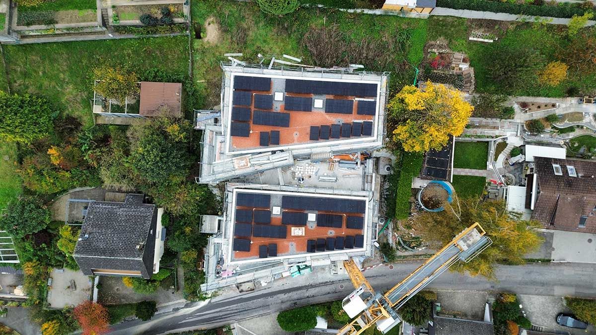 Luftaufnahme von zwei Wohnhäusern mit Solaranlagen auf den Dächern, umgeben von Bäumen und einem Baukran.