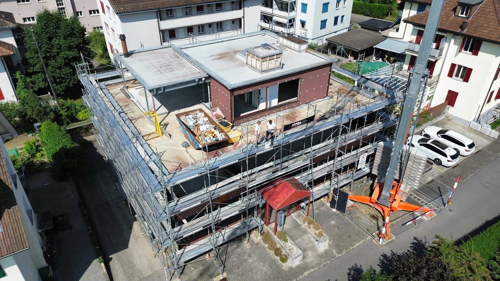 Luftaufnahme eines im Umbau befindlichen Gebäudes, umgeben von einem Metallgerüst, in dessen Nähe ein Baukran geparkt ist.