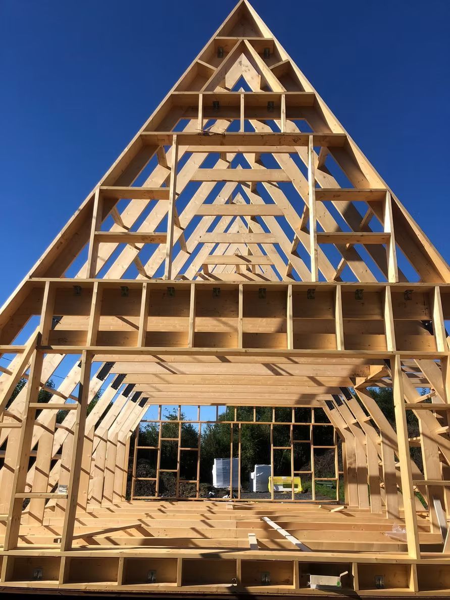Ein im Bau befindliches hölzernes A-förmiges Haus vor strahlend blauem Himmel.