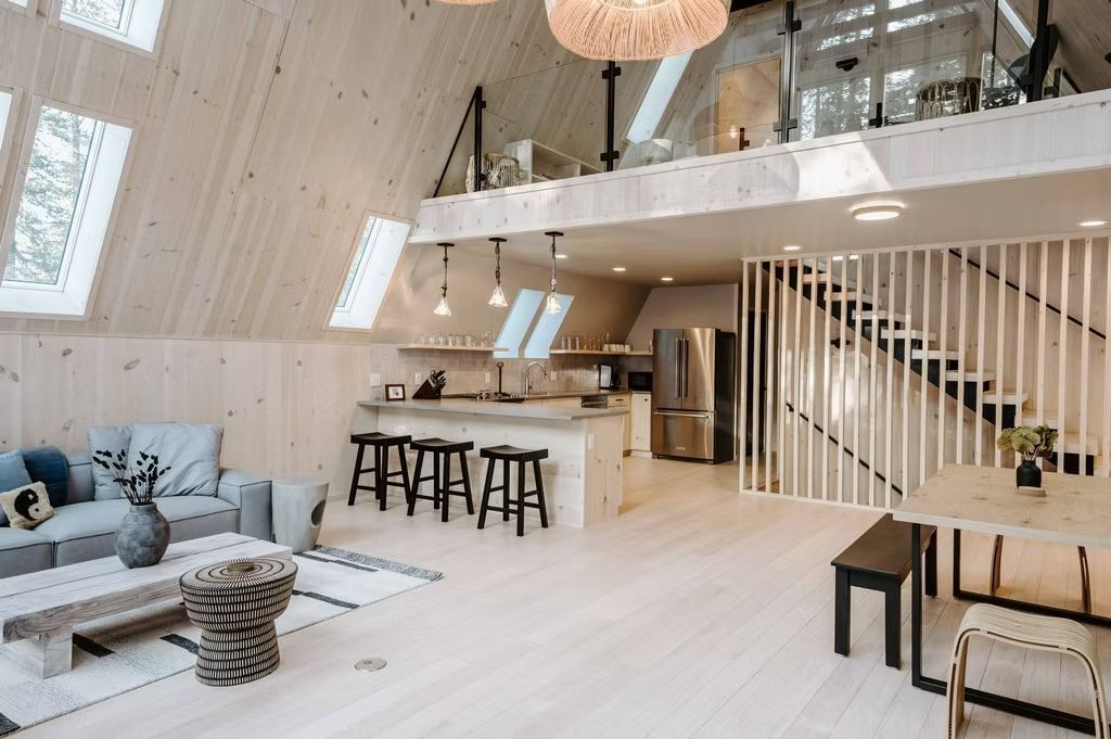 Modernes A-Rahmen-Hausinterieur mit hellen Holzoberflächen, offener Küche, Essbereich und einer Galerieebene.