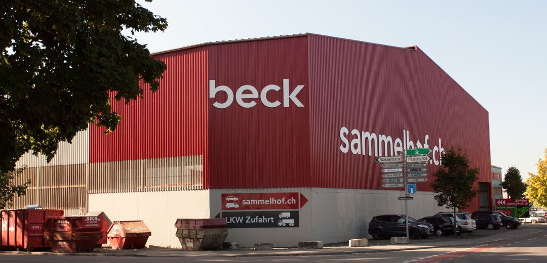 Eine große, rote Industriehalle für 'beck sammelhof.ch' mit roten Müllcontainern im Vordergrund.