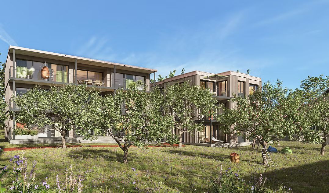 Ein moderner, zweistöckiger Apartmentkomplex mit Balkonen, eingebettet hinter einem üppig grünen Obstgarten unter strahlend blauem Himmel.