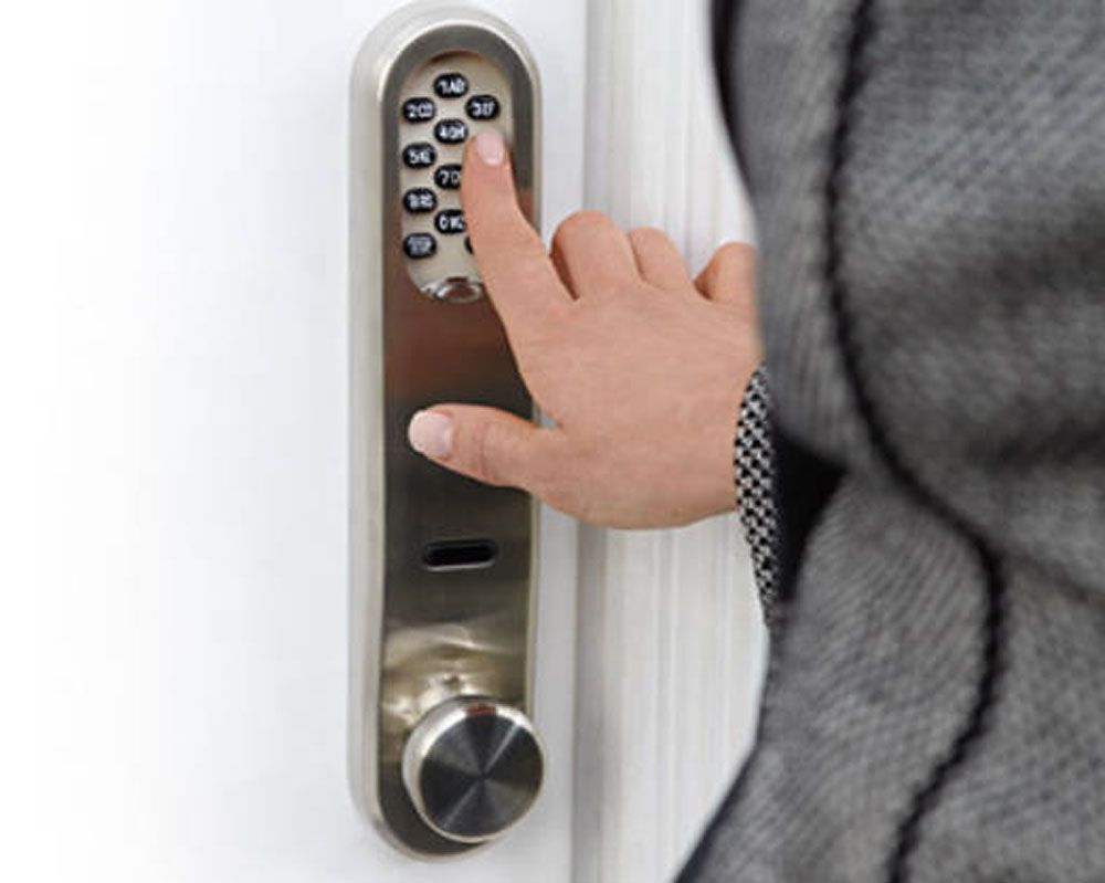 Der Finger einer Person gibt einen Code in ein silbernes Türschloss mit Tastatur ein.