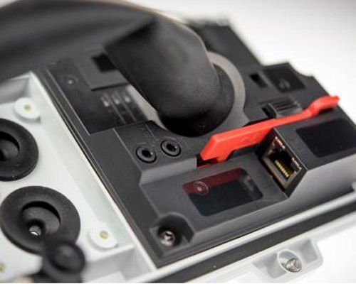 Nahaufnahme eines Geräts im Zusammenbau. Schwarze Komponenten mit einem roten Hebel und einem Ethernet-Anschluss sind zu sehen. Eine Hand mit einem schwarzen Handschuh ist zu sehen.