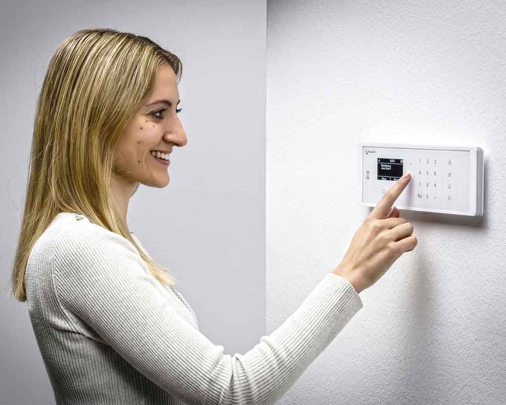 Lächelnde Frau, die eine weiße Tastatur eines Sicherheitssystems an einer weißen Wand verwendet.