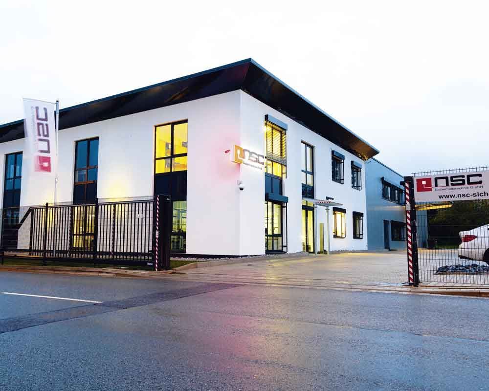 Weißes und graues zweistöckiges Gebäude mit dem NSC-Logo, einer Flagge und einem Tor; Außenaufnahme.