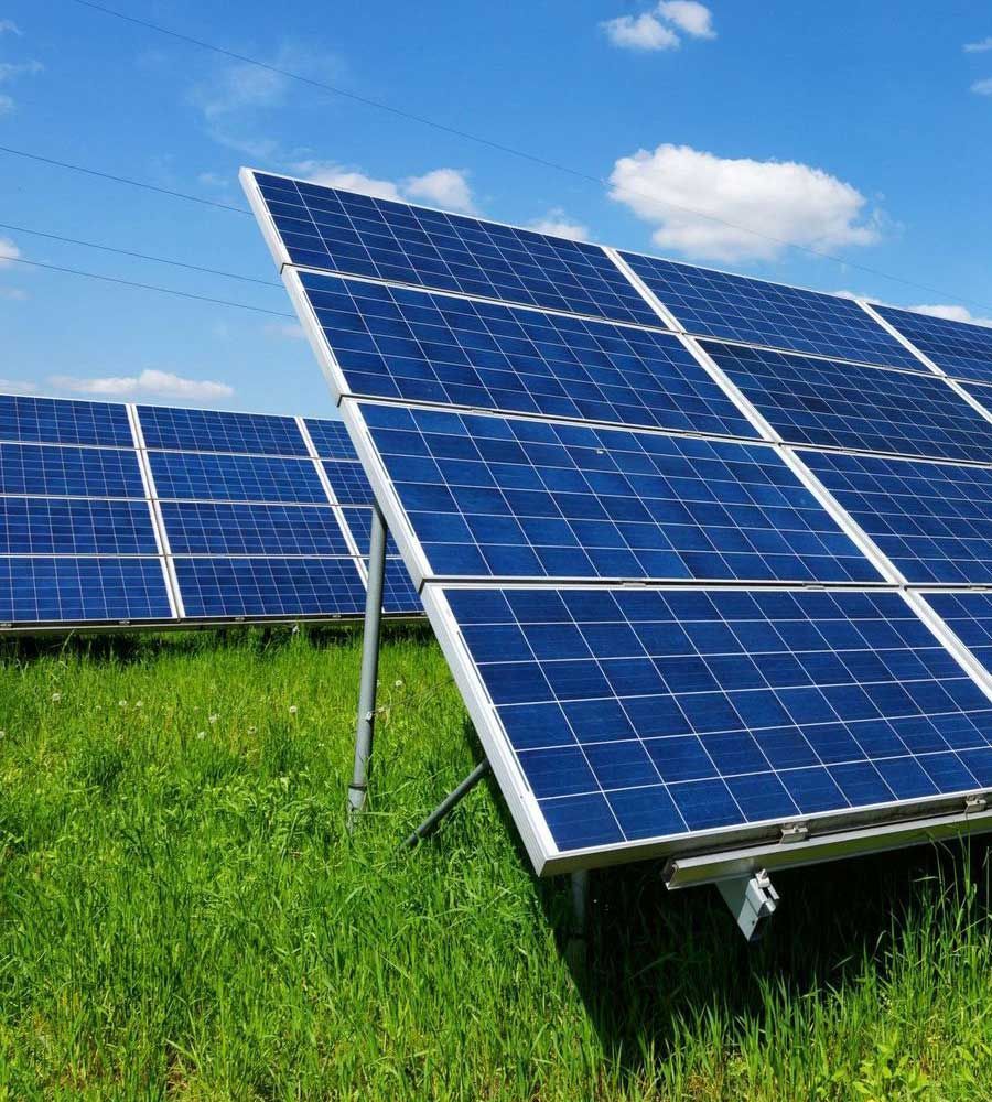 Paneles solares en un campo verde bajo un cielo azul con nubes blancas esponjosas.
