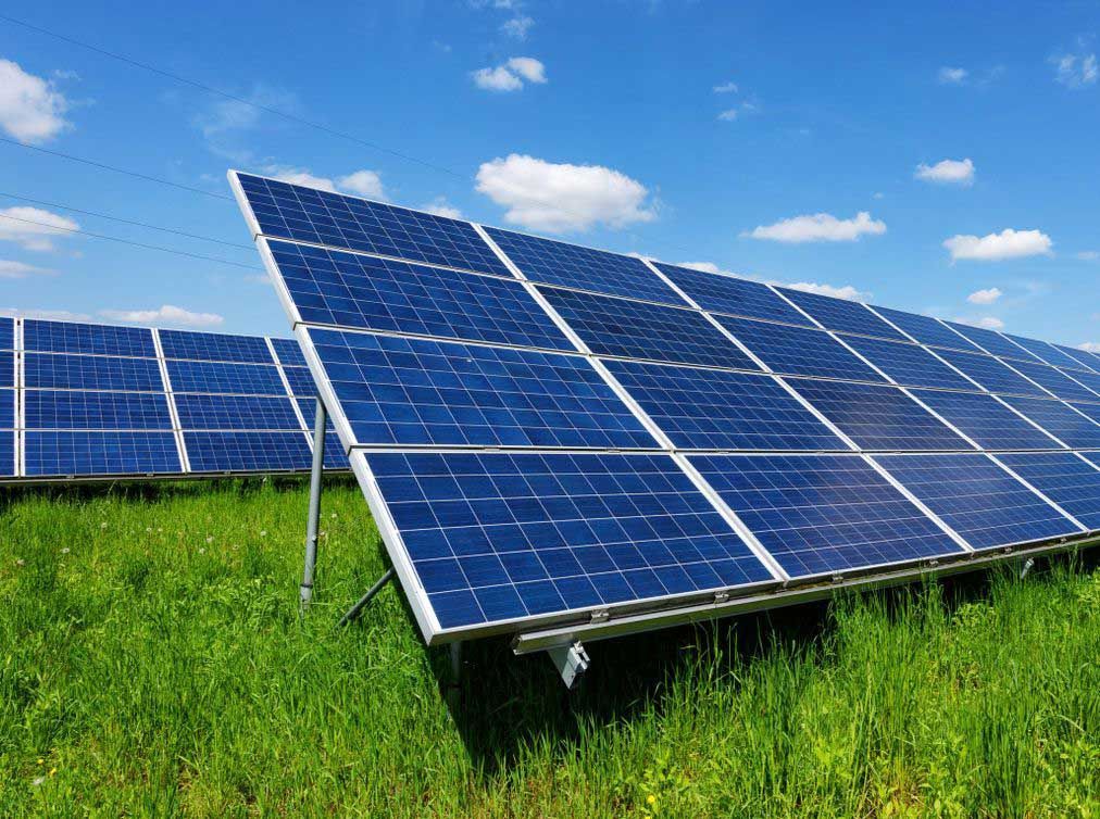 Paneles solares en un campo de césped verde contra un cielo azul con nubes blancas esponjosas.