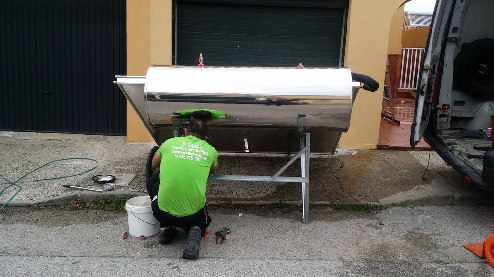 Persona con camisa verde trabajando en un gran contenedor de acero inoxidable montado sobre un soporte de metal al aire libre.