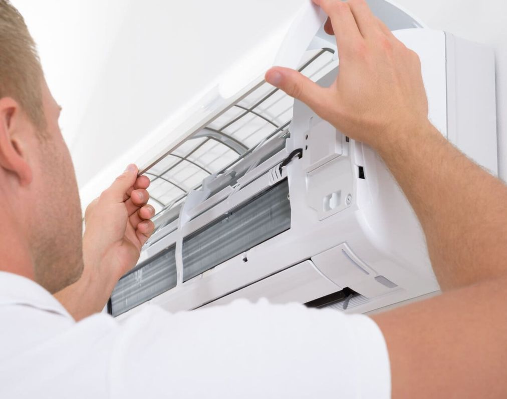 Persona limpiando una unidad de aire acondicionado; sacando el filtro.