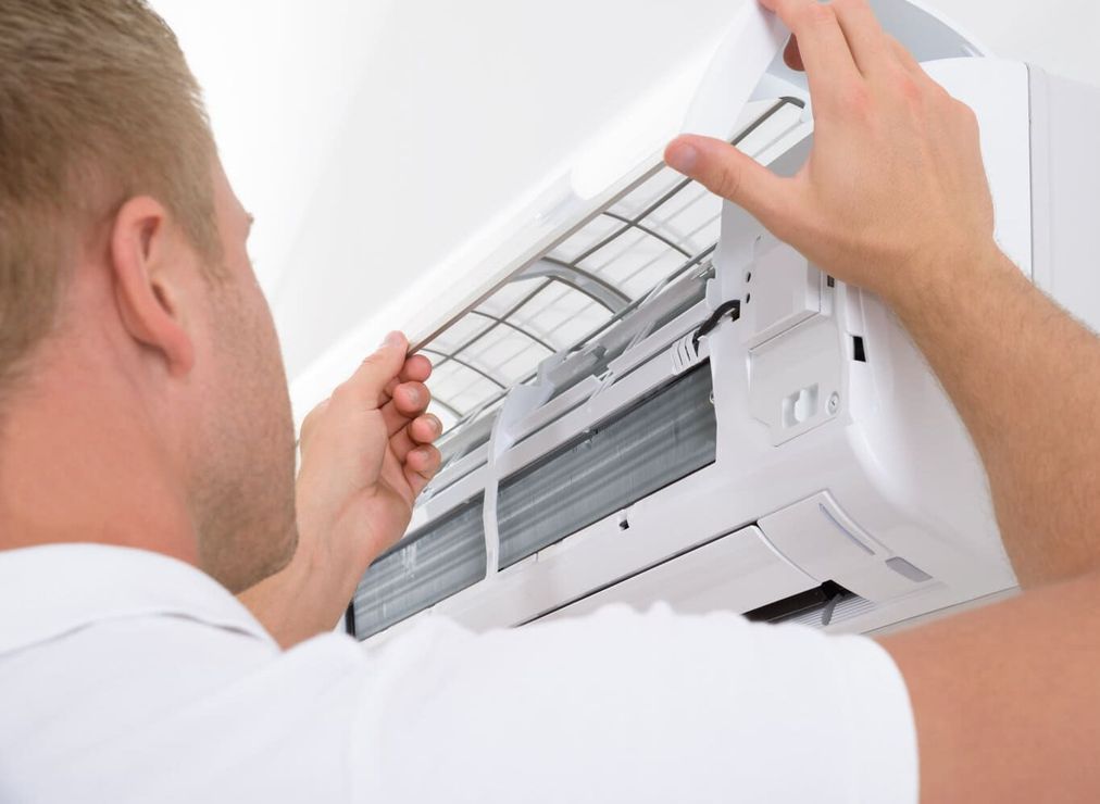 Hombre reemplazando un filtro de aire acondicionado en una unidad de pared blanca.