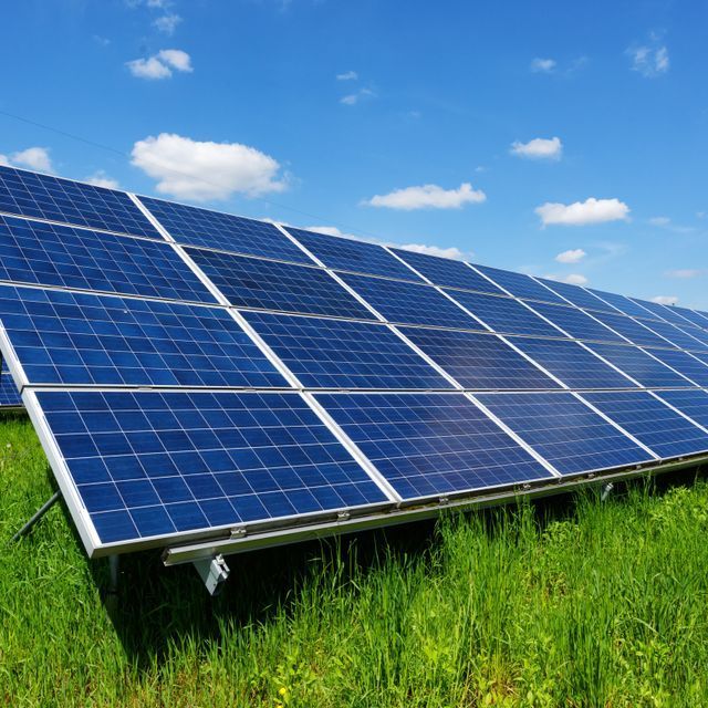 Paneles solares sobre césped verde bajo un cielo azul con nubes blancas esponjosas.