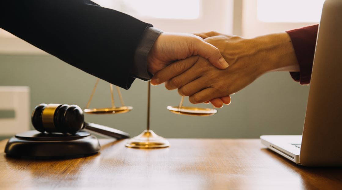 Manos temblando sobre una balanza de justicia, una computadora portátil y un mazo sobre un escritorio de madera.