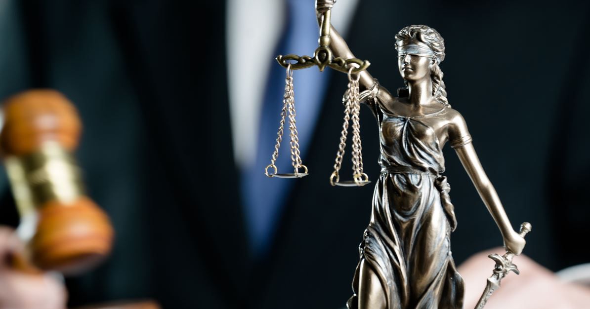 Estatua de la Dama de la Justicia con balanza y espada; juez al fondo sosteniendo un mazo.