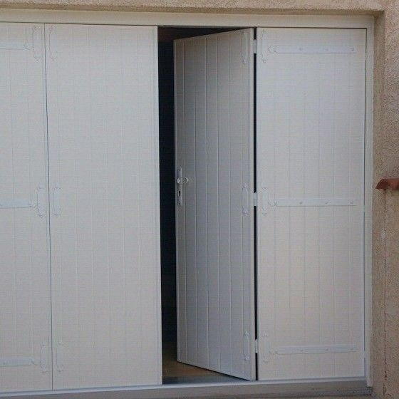 Portes de garage pliantes blanches partiellement ouvertes, placées dans un cadre en béton de couleur claire.