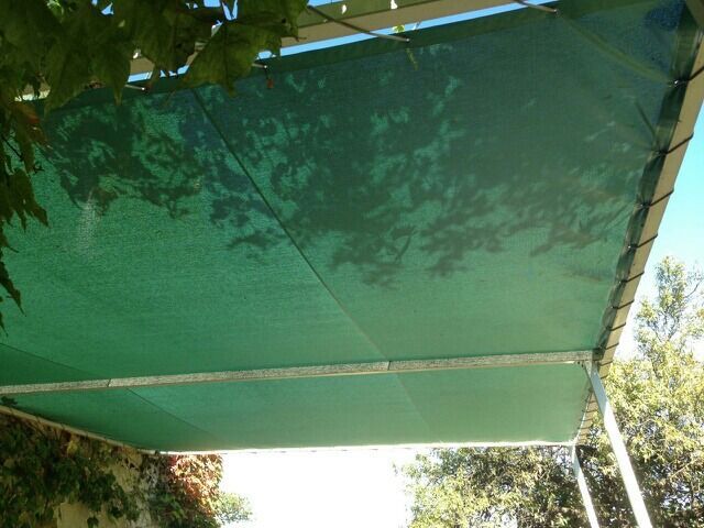 Toile d'ombrage verte recouvrant une pergola à ossature métallique ; la lumière du soleil filtre à travers.