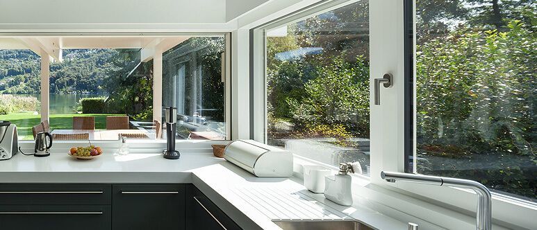 Eine Küche mit Spüle, Wasserhahn und großen Fenstern.