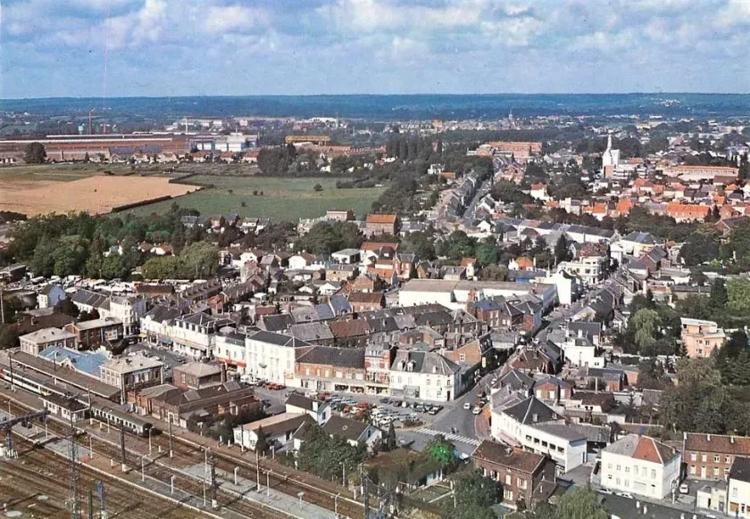 Vue aérienne d'une petite ville avec des maisons, des champs et des voies ferrées sous un ciel dégagé.
