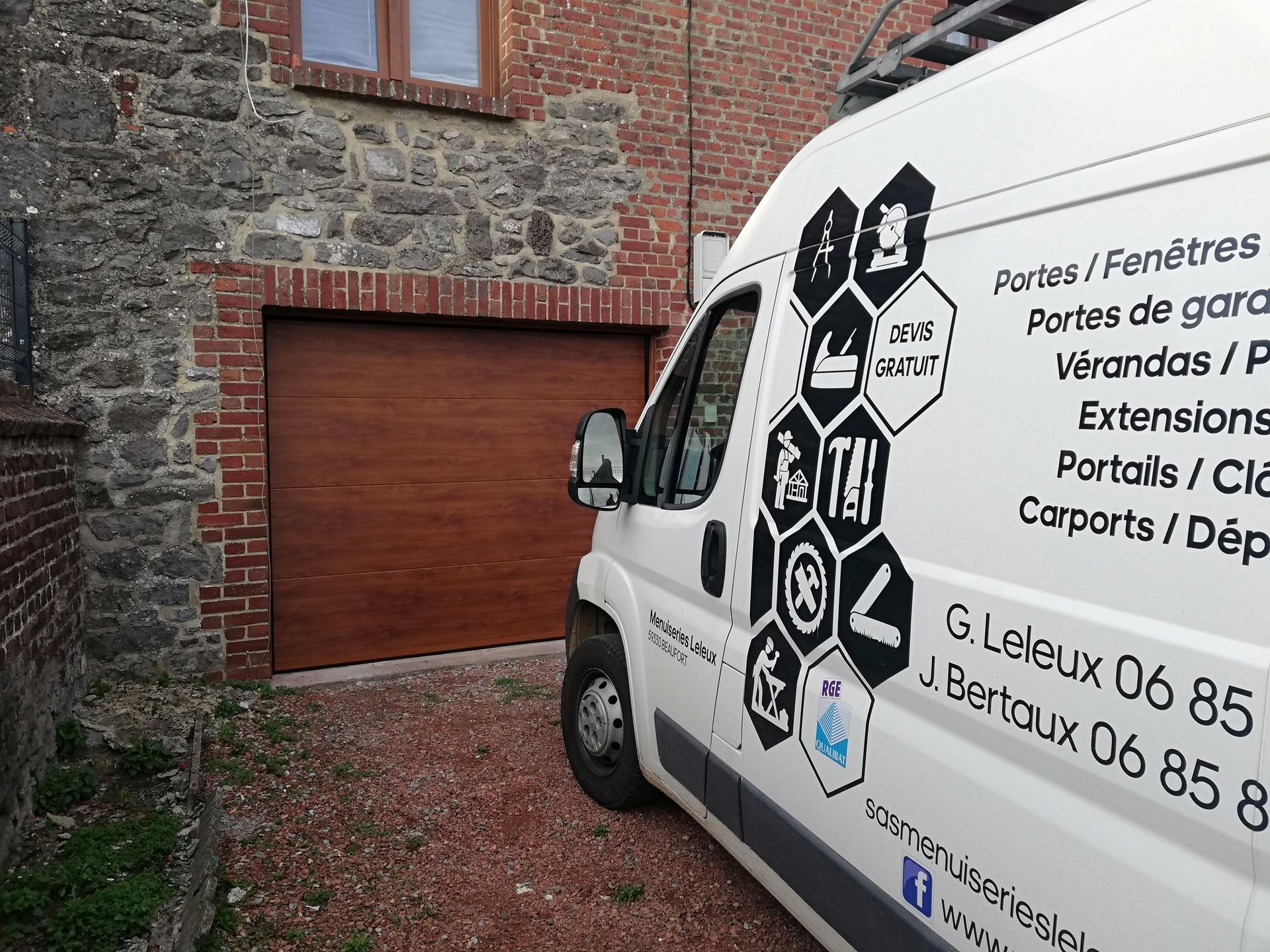 Une camionnette blanche arborant une enseigne de rénovation française est garée à côté d'un bâtiment en briques et en pierres avec une porte de garage rouge.
