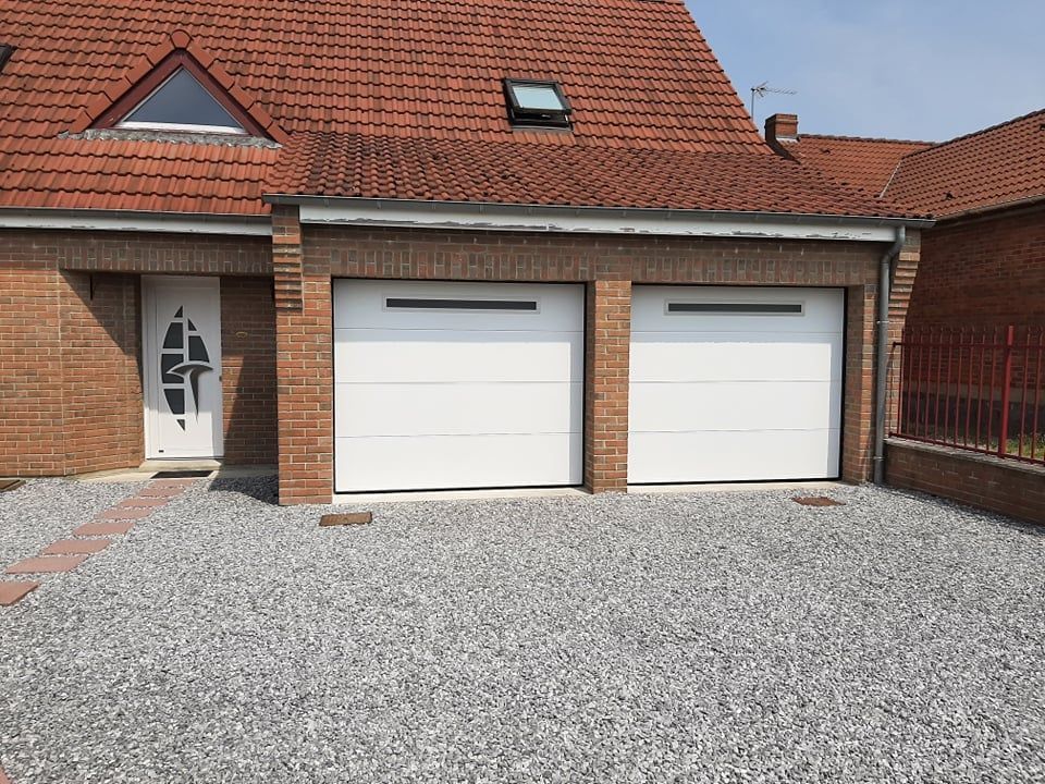 Façade de maison en briques avec deux portes de garage blanches, une porte d'entrée principale et une allée en gravier.