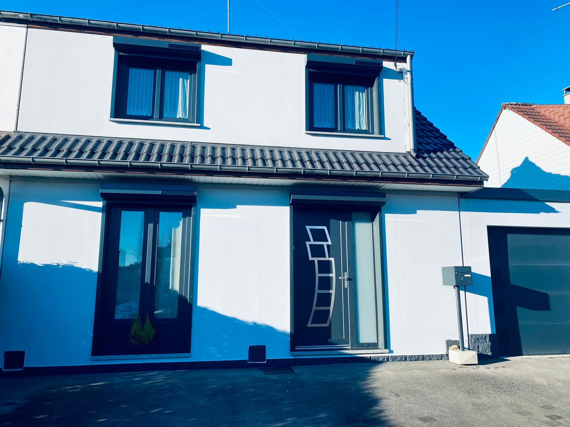 Maison moderne blanche à deux étages avec des boiseries bleu foncé et un garage en façade sous un ciel d'un bleu éclatant