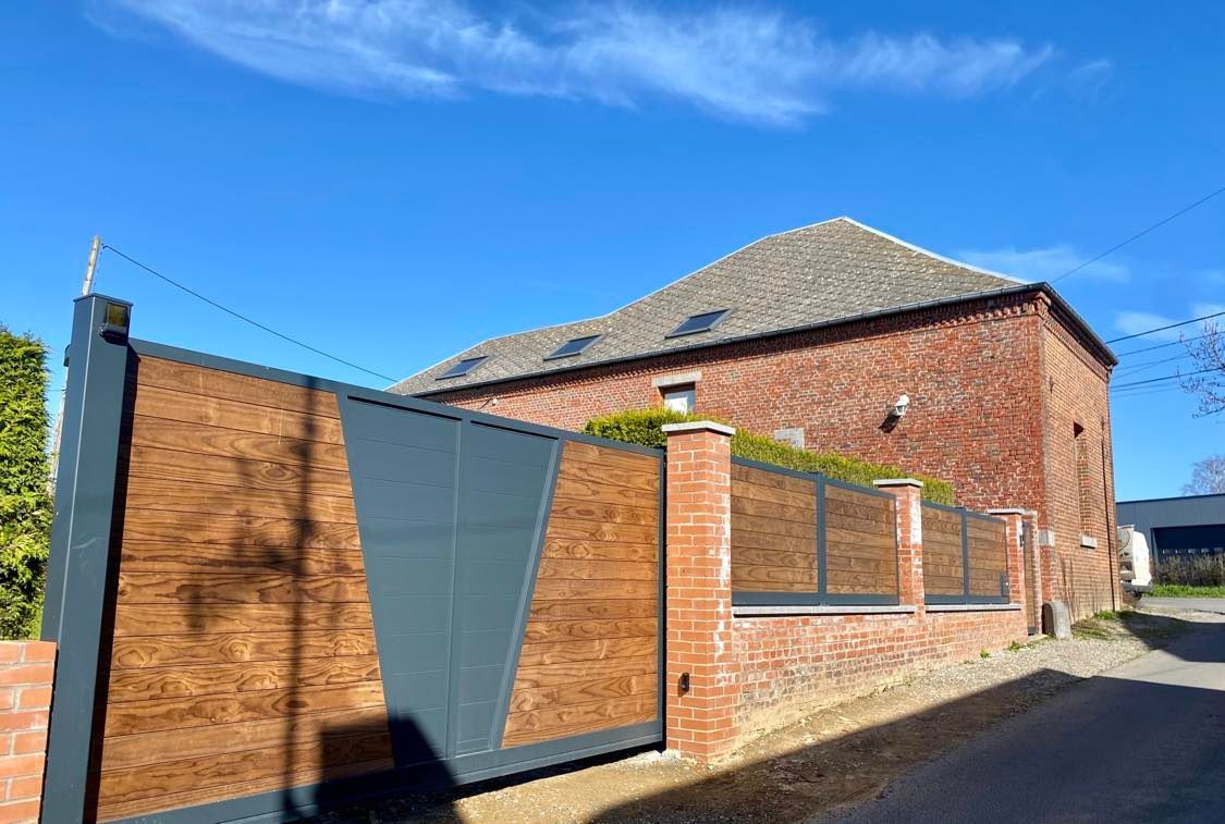 Maison en briques avec un toit de tuiles, un portail en métal et un ciel bleu au-dessus.