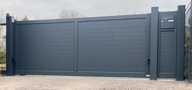 Portail coulissant en métal gris foncé avec poteaux latéraux assortis, le long d'une allée ou d'une entrée de propriété.