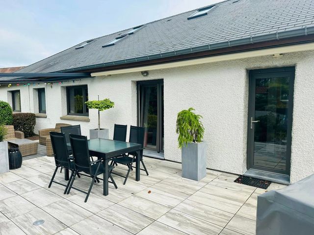 Terrasse avec table à manger noire, chaises, plantes en pot et façade d'une maison en pierre claire avec toit de tuiles foncées.