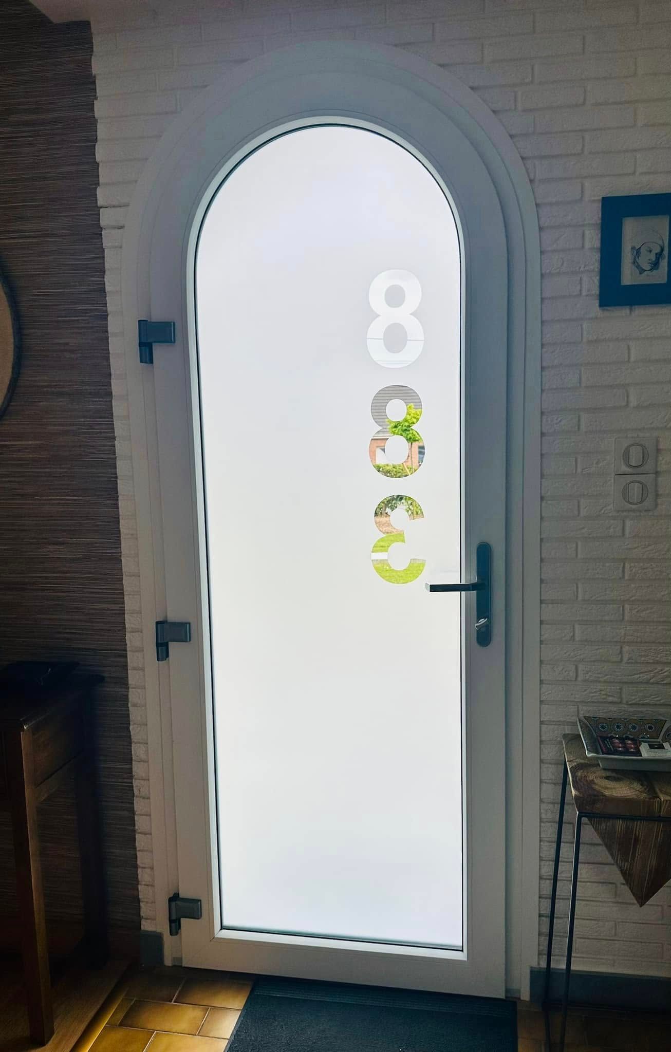 Porte cintrée en verre dépoli dans un mur de briques, avec une poignée noire et les chiffres 8, 3, 6 sur le verre.