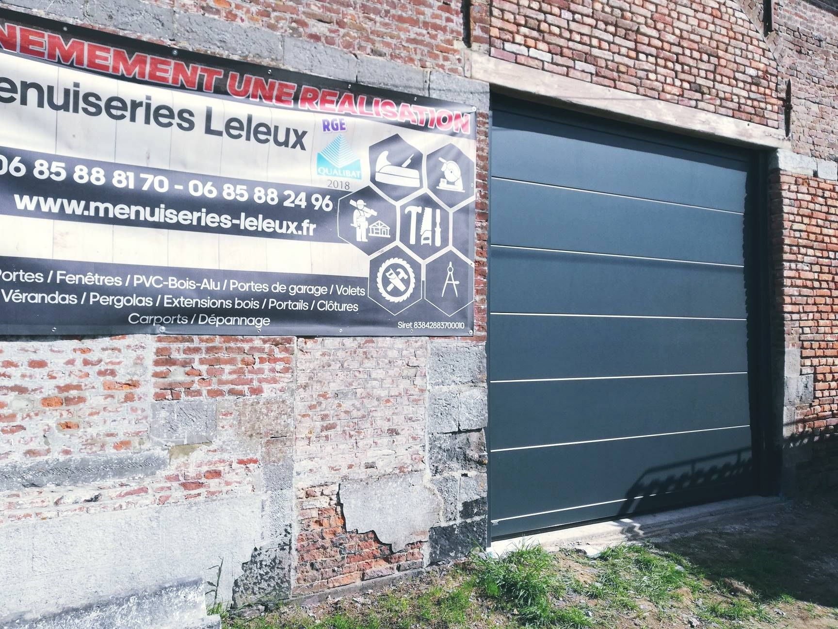 Panneau Maçonnerie Leleux sur un mur de briques à côté d'une porte de garage sombre