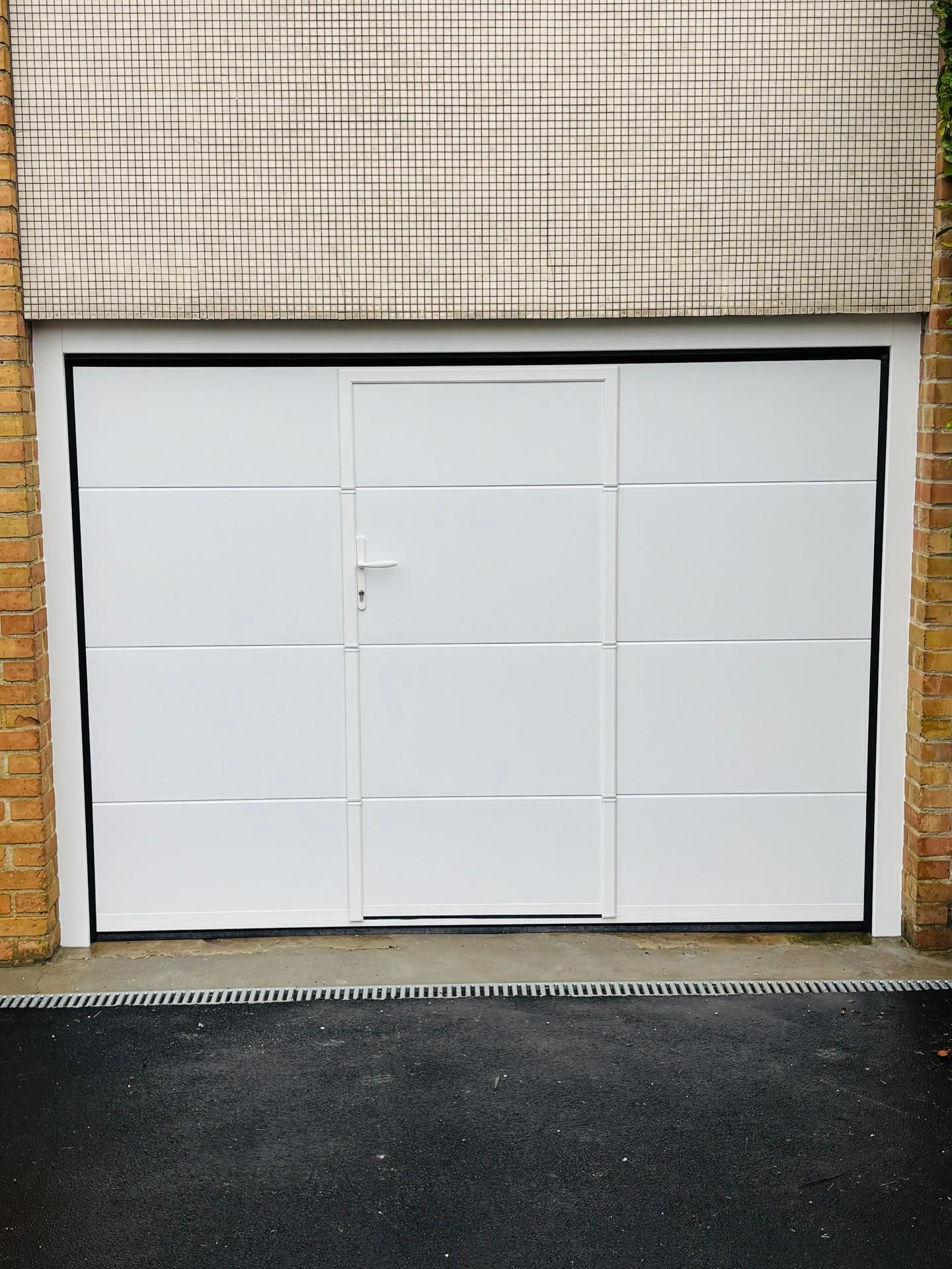 Porte de garage blanche encastrée dans un mur de briques au-dessus d'une allée pavée sombre.
