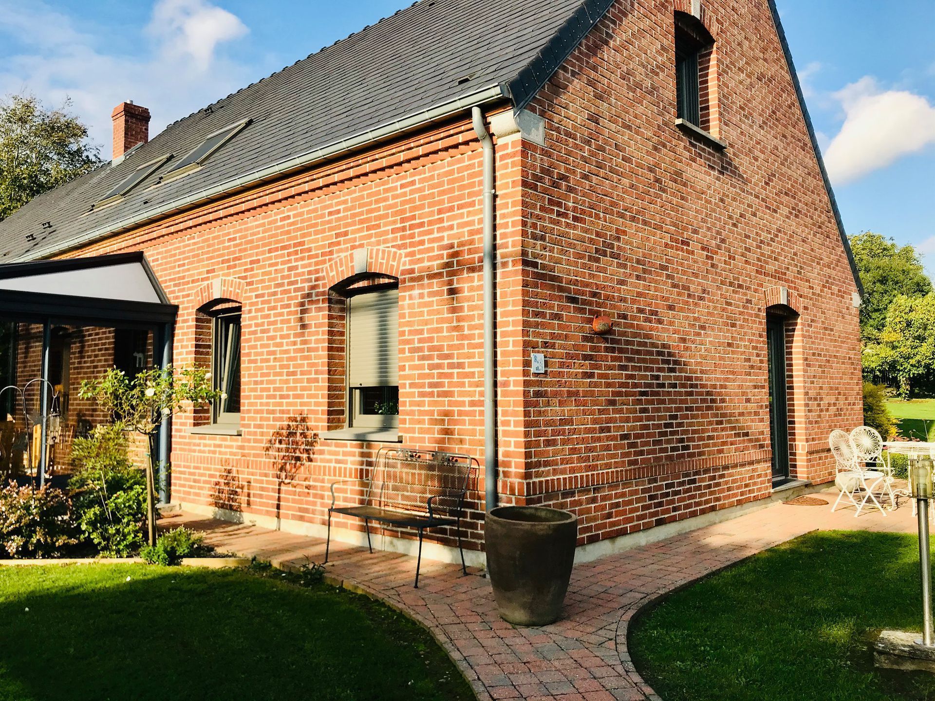 Maison en briques avec toit sombre, fenêtres à encadrement noir et petit chemin de jardin devant.
