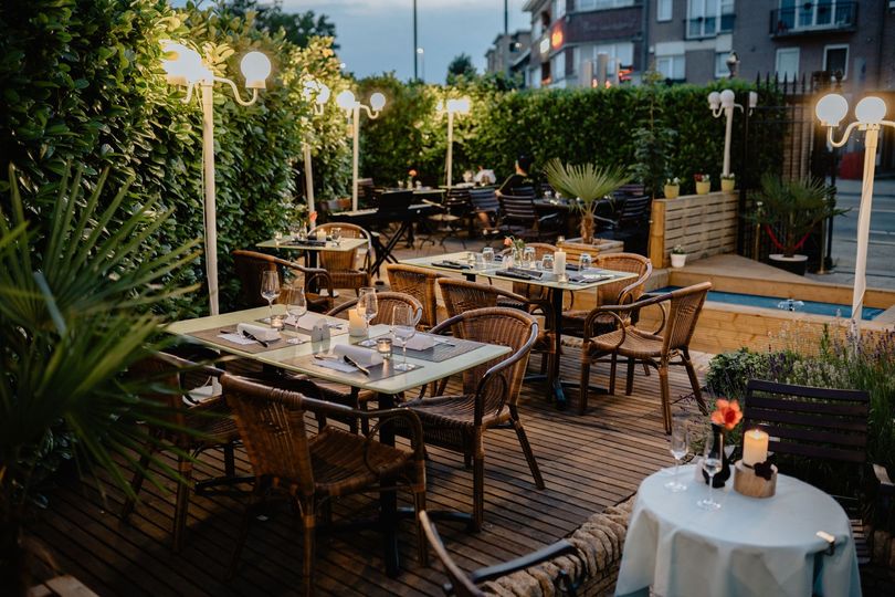 Terrasse de restaurant en plein air avec des tables dressées, des chaises en osier et des guirlandes lumineuses chaleureuses au crépuscule