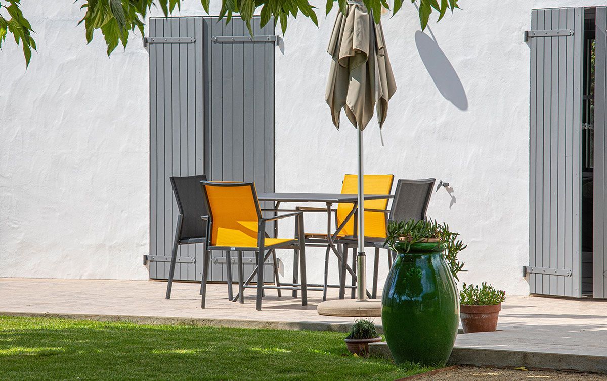 Salon de jardin avec des chaises jaunes sur une terrasse avec des volets.