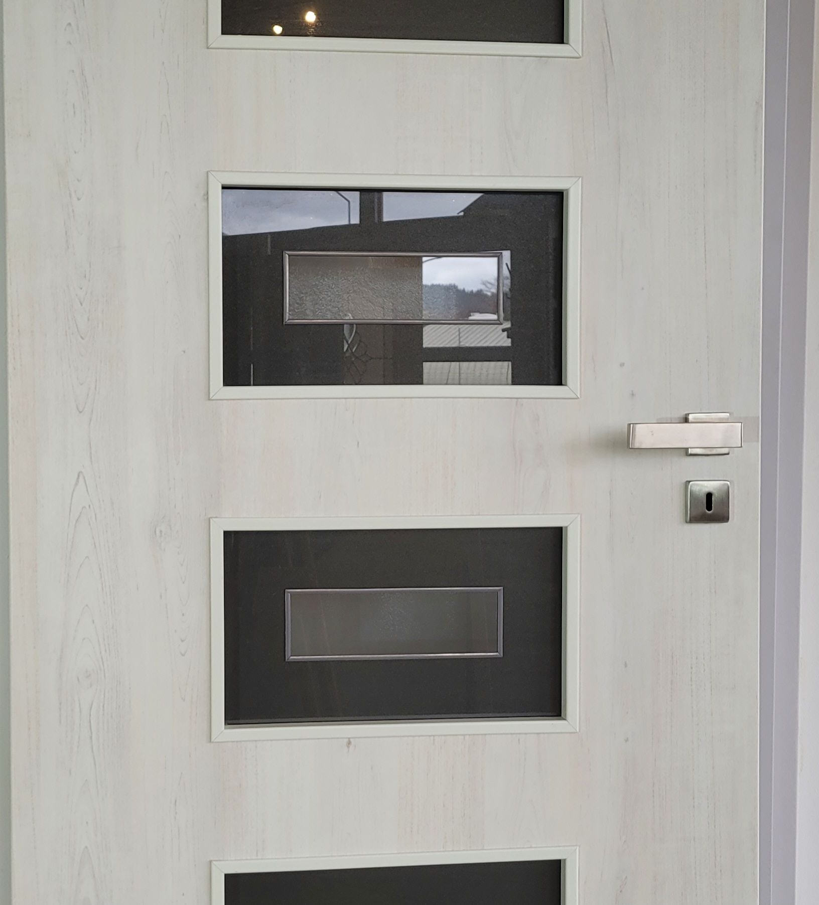 Eine weiße Tür mit drei Fenstern und einem Edelstahlgriff.