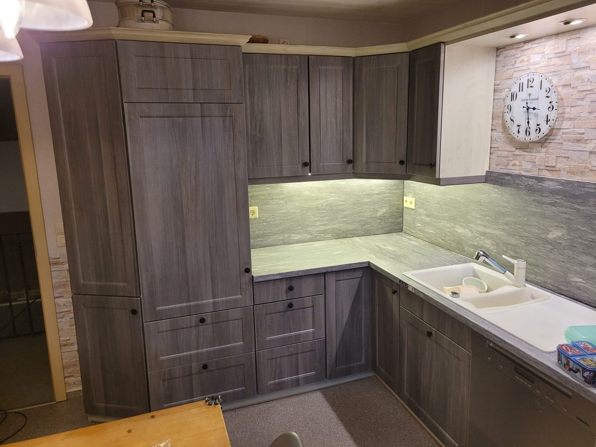 Eine Küche mit grauen Schränken und einer Uhr an der Wand.
