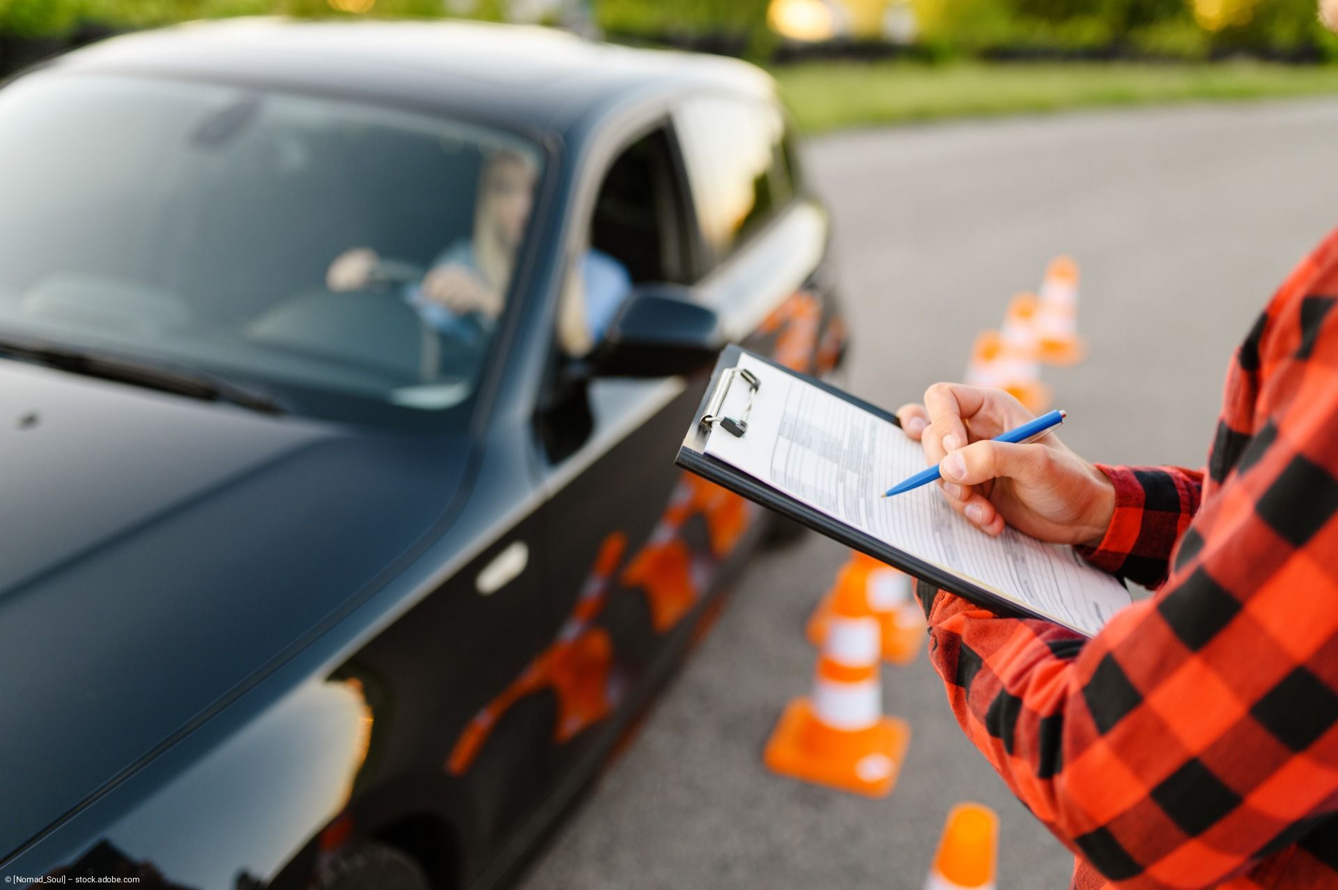 Ein Fahrer verfasst einen Verkehrsbericht neben einem schwarzen Auto und orangefarbenen Pylonen.