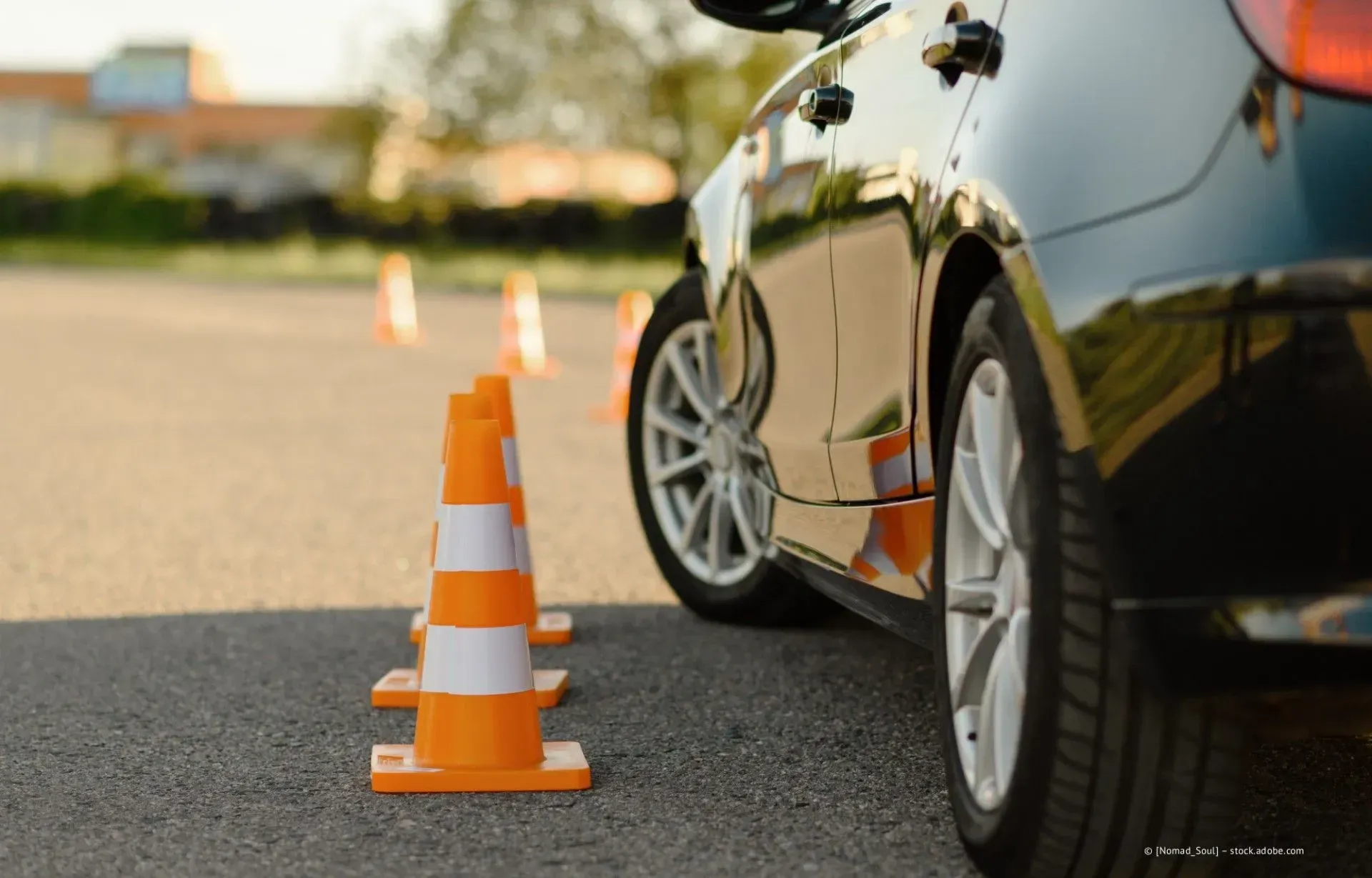 Orangefarbene Verkehrskegel neben einem geparkten schwarzen Auto auf einer Fahrbahn.